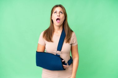 Orta yaşlı, kırık kollu, izole edilmiş arka planda askı takan yukarı bakan ve şaşırmış bir ifadeyle.