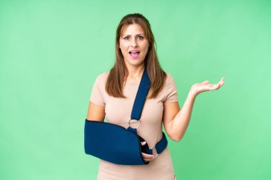 Orta yaşlı, kırık kollu ve izole edilmiş bir arkaplanda askı takıyor ve şok olmuş bir yüz ifadesi var.