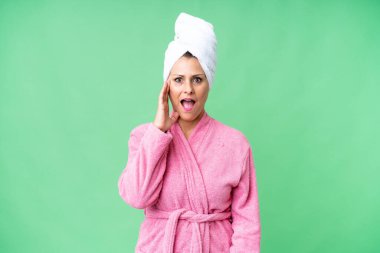Yüzü şoke olmuş ve şaşırmış bir şekilde münzevi bir arka planda bornoz giymiş orta yaşlı beyaz kadın.