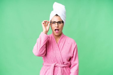 Bornozlu orta yaşlı beyaz kadın izole edilmiş arka planda gözlüklü ve şaşırmış.