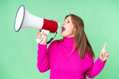 Middle age woman over isolated background shouting through a megaphone to announce something in lateral position