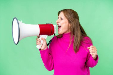 Middle age woman over isolated background shouting through a megaphone to announce something in lateral position