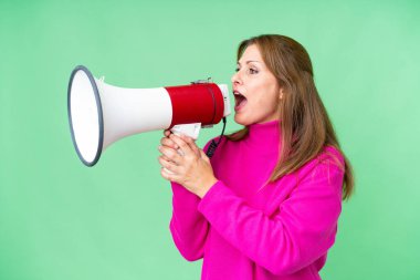 Middle age woman over isolated background shouting through a megaphone to announce something in lateral position