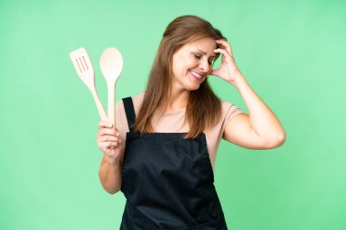 Orta yaşlı, beyaz bir kadın izole bir arka planda elinde oklavayla gülümsüyor.