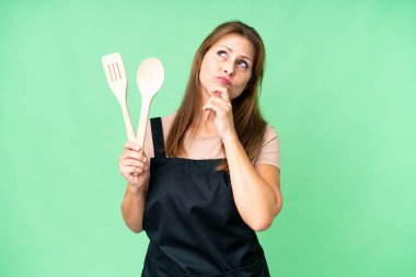 Orta yaşlı, beyaz bir kadın izole bir arka planda elinde oklavayla yukarı bakıyor.