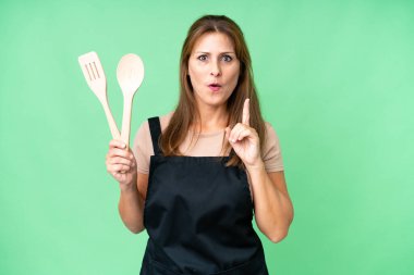 Orta yaşlı, beyaz bir kadın, izole edilmiş arka planda bir iğne tutuyor. Çözümü bulmak için parmağını kaldırıyor.