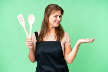 Orta yaşlı, beyaz bir kadın, izole edilmiş arka planda bir rozet tutuyor. Davet etmek için ellerini yana uzatıyor.