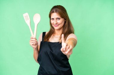 Orta yaşlı, beyaz bir kadın, izole edilmiş arka planda elinde oklavayla parmağını kaldırıyor.