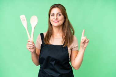 Orta yaşlı, beyaz bir kadın, izole edilmiş arka planda bir iğne tutuyor ve en iyinin işareti olarak parmağını kaldırıyor.