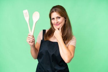 Orta yaşlı, beyaz bir kadın izole bir arka planda elinde oklavayla mutlu ve gülümsüyor.