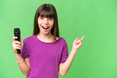 Küçük şarkıcı kız izole edilmiş bir arka planda mikrofonu eline aldı. Şaşırdı ve işaret etti.