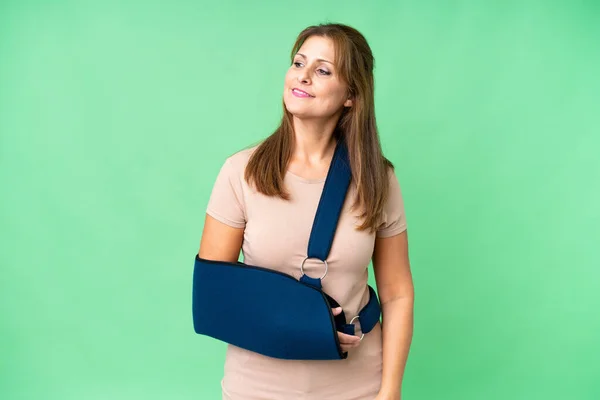 stock image Middle age with broken arm and wearing a sling over isolated background looking to the side and smiling