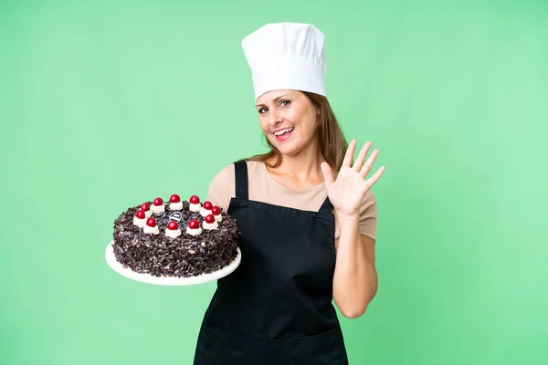 Mulher Chef Pastelaria Meia Idade Segurando Grande Bolo Sobre Fundo — Fotografia de Stock