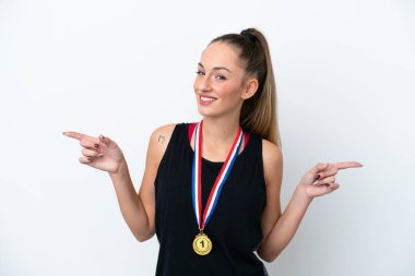Beyaz arka planda izole edilmiş beyaz madalyalı genç beyaz kadın parmak uçlarını işaret ediyor ve mutlu.