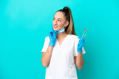 Kafkasyalı dişçi, elinde mavi arka planda izole edilmiş aletlerle yukarı bakarken bir fikir üretiyor.