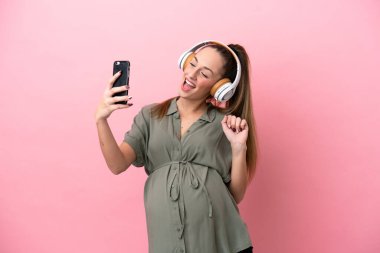 Pembe arka planda izole edilmiş genç bir kadın hamile ve selfie çekiyor.