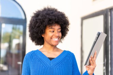 Afro-Amerikalı bir kız açık havada mutlu bir ifadeyle bir tablet tutuyor.