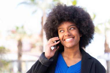 Afro-Amerikalı kız dışarıda cep telefonuyla birileriyle sohbet ediyor.