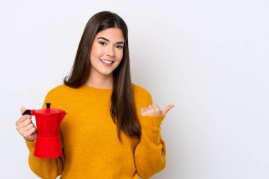 Beyaz arka planda izole edilmiş kahve makinesini tutan genç Brezilyalı kadın bir ürünü sunmak için kenarı işaret ediyor.