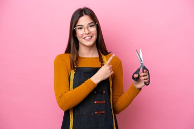 Pembe arka planda izole edilmiş genç Brezilyalı terzi bir ürünü sunmak için kenarı işaret ediyor.
