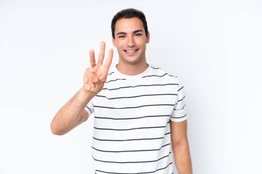 Beyaz arka planda izole edilmiş genç beyaz adam mutlu ve parmaklarıyla üçe kadar sayıyor.