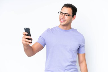 Beyaz arka planda izole edilmiş genç beyaz bir adam selfie çekiyor.