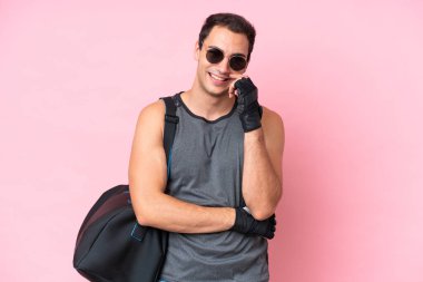 Spor çantalı genç beyaz adam pembe arka planda gözlüklü ve mutlu.