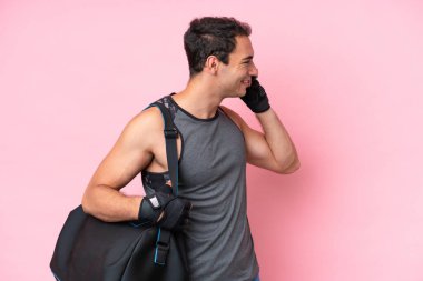 Spor çantalı genç beyaz adam pembe arka planda izole edilmiş cep telefonuyla biriyle sohbet ediyor.