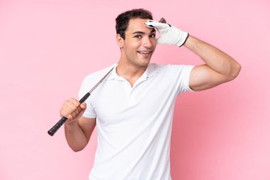 Pembe arka planda izole edilmiş genç golfçü yan tarafa bakarken sürpriz jest yapıyor.