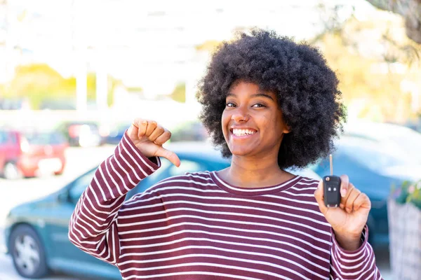 African American girl holding car keys at outdoors proud and self-satisfied