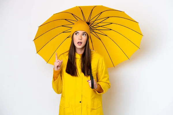 若いですブラジル人女性でレインプルーフコートと傘は白い背景に隔離されています指を指すアイデアを考えます — ストック写真