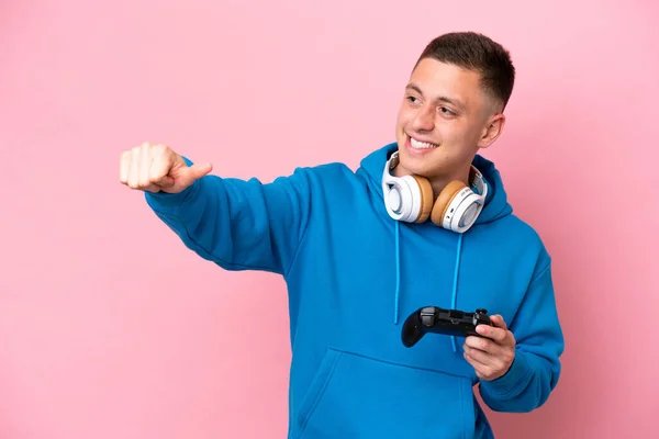 一个年轻的巴西男人在玩一个用粉色背景隔离的电子游戏控制器 他举起了一个大拇指 — 图库照片