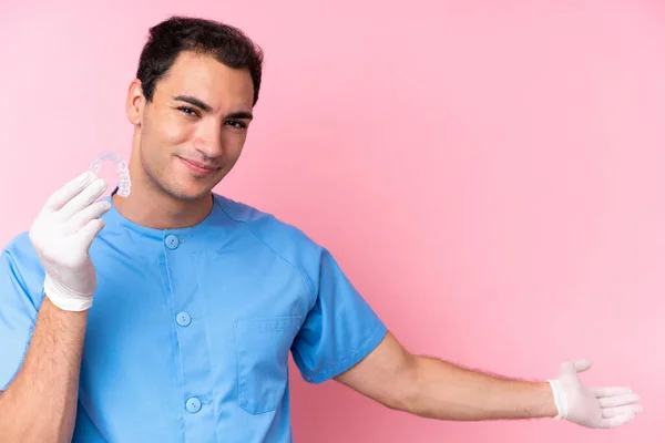 Dentist caucasian man holding invisible braces isolated on pink background extending hands to the side for inviting to come
