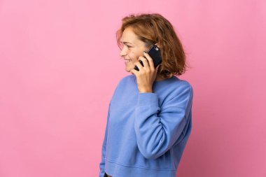 Genç Gürcü kadın pembe arka planda izole edilmiş cep telefonuyla biriyle sohbet ediyor.