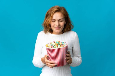 Genç Gürcü bir kadın mavi arka planda izole edilmiş. Elinde koca bir kova patlamış mısır var.