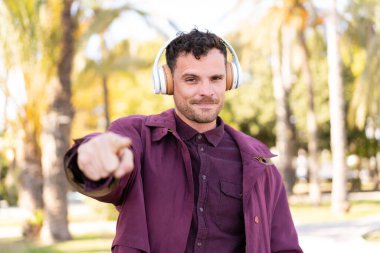 Genç beyaz bir adam açık havada müzik dinliyor.