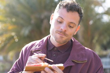 Beyaz bir adam açık havada saşimi yiyor.