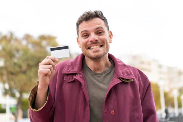 Młody Biały Mężczyzna Trzymając Kartę Kredytową Świeżym Powietrzu Zaskoczeniem Wstrząśnięty — Zdjęcie stockowe