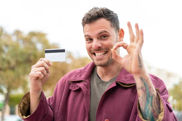 Mladý Běloch Který Venku Drží Kreditní Kartu Ukazující Prstem Ceduli — Stock fotografie