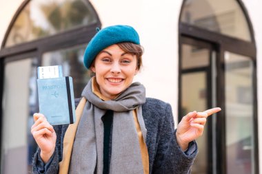 Açık havada elinde pasaport tutan esmer kadın şaşırdı ve parmağını yana çevirdi.