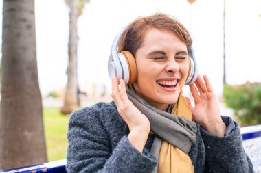 Esmer kadın açık havada müzik dinliyor ve şarkı söylüyor.