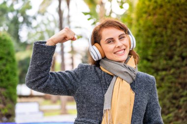 Açık havada müzik dinleyen esmer bir kadın güçlü bir jest yapıyor.