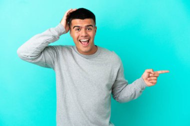 Soyutlanmış mavi arka planda genç yakışıklı adam şaşırdı ve parmağını yana çevirdi.