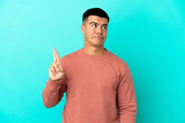 Young handsome man over isolated blue background with fingers crossing and wishing the best