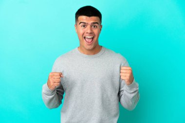 Soyutlanmış mavi arka planda genç yakışıklı adam galibiyeti kutluyor.