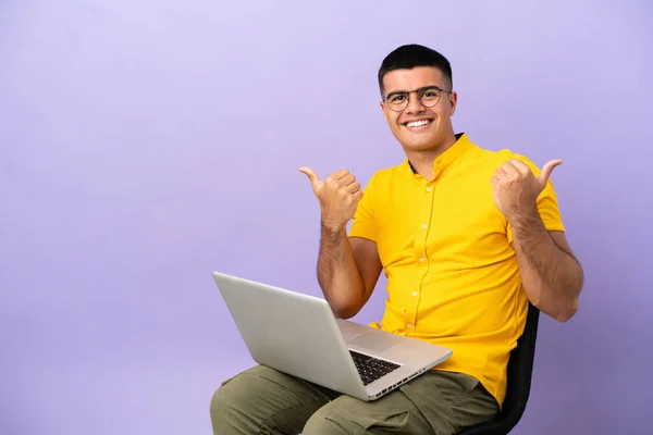 stock image Young man sitting on a chair with laptop with thumbs up gesture and smiling