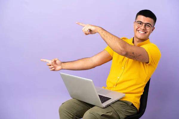 Jovem Sentado Uma Cadeira Com Laptop Apontando Dedo Para Lado — Fotografia de Stock