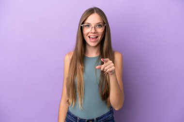 Mor arka planda izole edilmiş genç Litvanyalı kadın şaşırmış ve ön tarafı işaret ediyor.