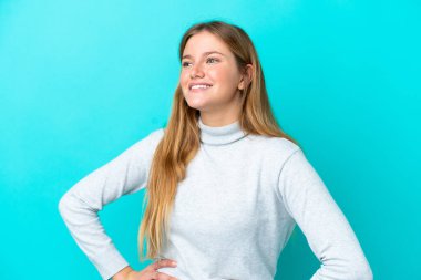 Mavi arka planda soyutlanmış genç sarışın kadın kolları kalçasında ve gülümsüyor.