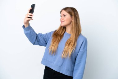 Beyaz arka planda izole edilmiş genç sarışın bir kadın selfie çekiyor.